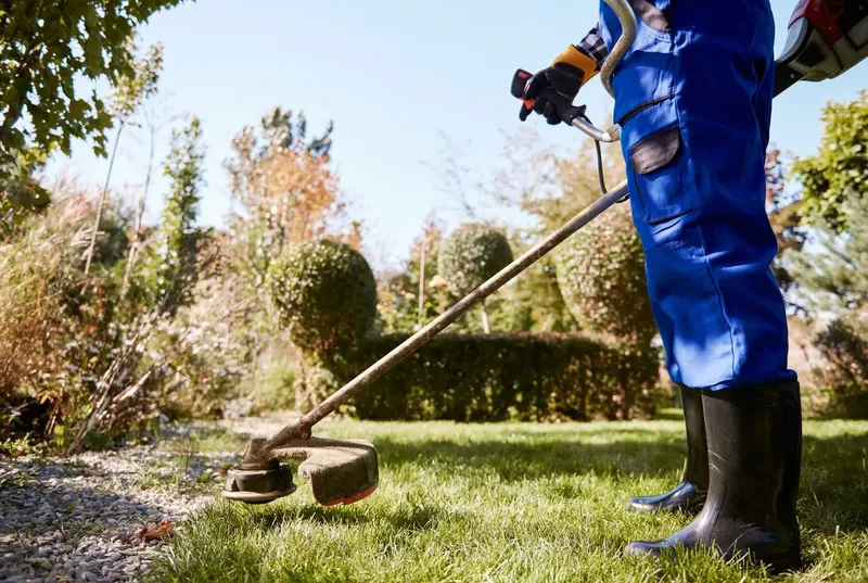 Especialista realizando mantenimiento de césped con desbrozadora en un jardín
